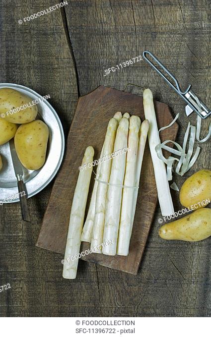 Fresh white asparagus with a peeler next to new potatoes