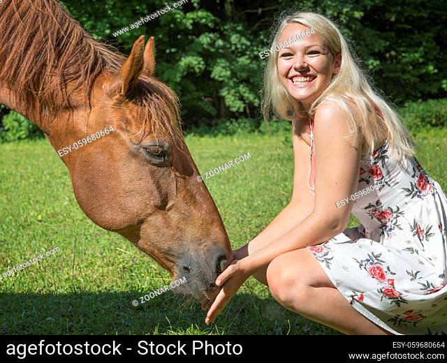 Junge hübsche Frau mit langen blonden Haaren beschäftigt sich mit ihrem Pferd