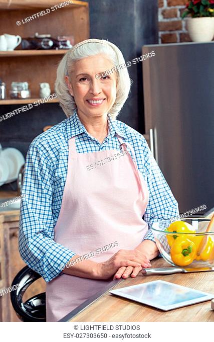Senior woman in apron smiling at camera in kitchen