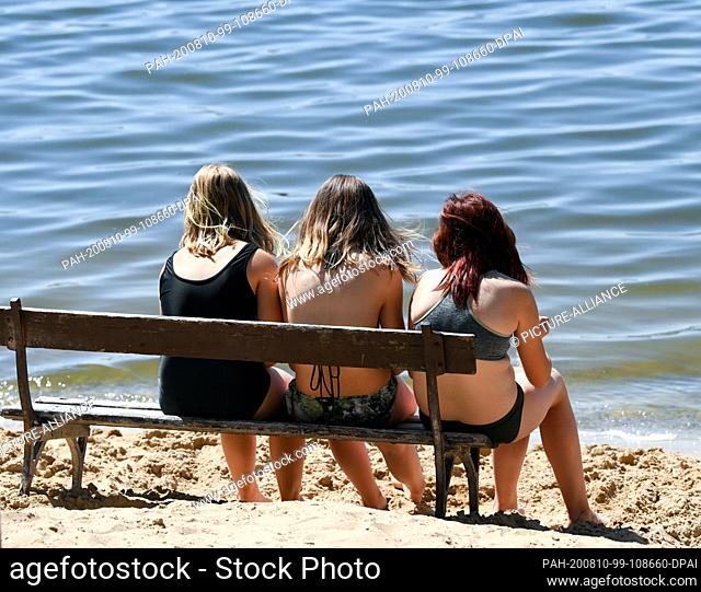 05 August 2020, Brandenburg, Mötzow: Three girls sit together on a bench by the water in the holiday resort in the Perspektivfabrik am Beetzsee