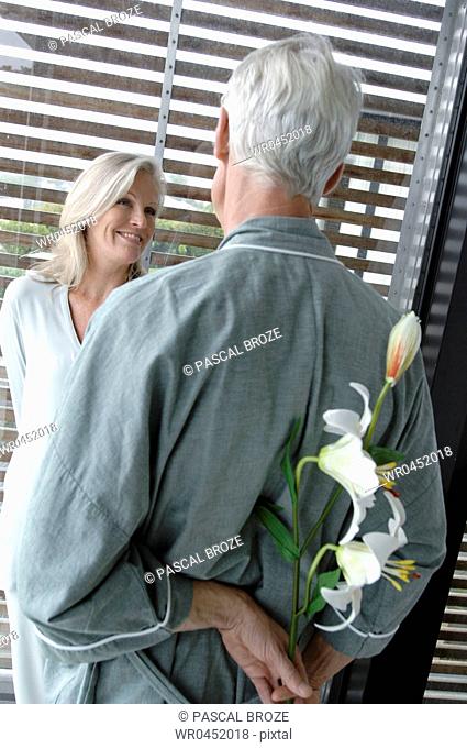 Rear view of a mature man hiding flowers behind his back with a mature woman looking at him