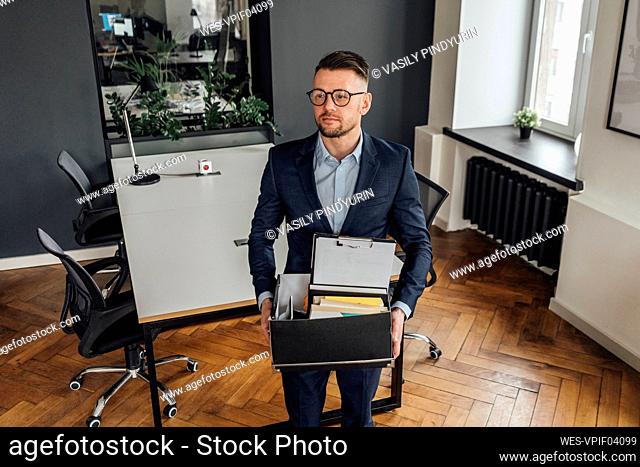 Thoughtful male entrepreneur holding belongings while standing at office
