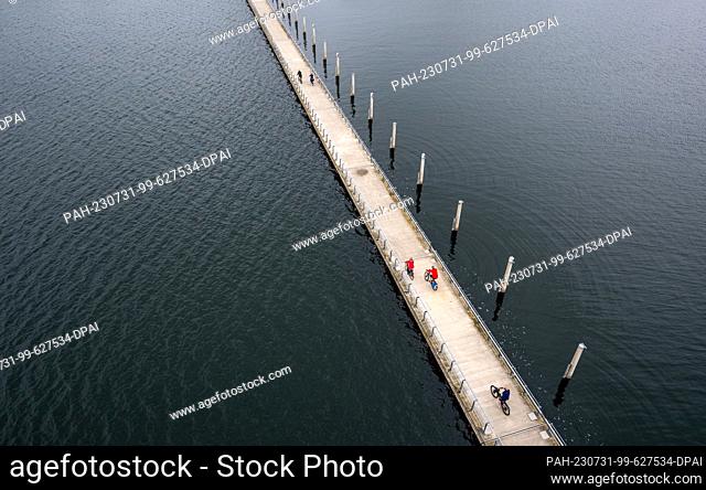 31 July 2023, Saxony-Anhalt, Bitterfeld-Wolfen: Cyclists are riding in the rain on a footbridge that leads across Lake Goitzsee to the 26-meter-high water level...