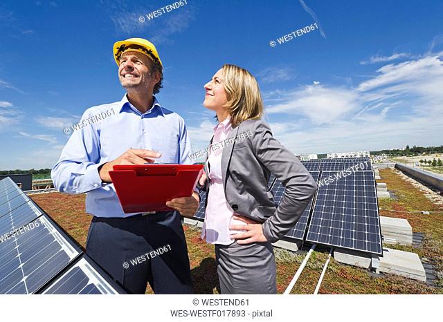 Germany, Munich, Engineers with clip board in solar plant, smiling
