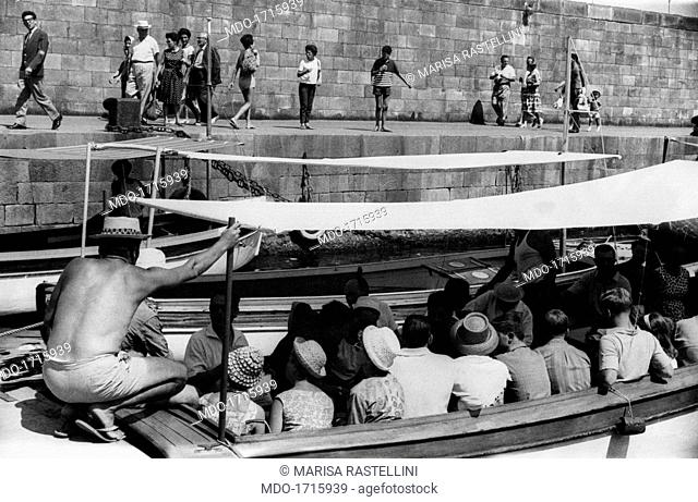 Tourists on board. Tourists on board a barge are waiting for setting out; a bare-chested chaperon is crouched on the hull, faced backwards