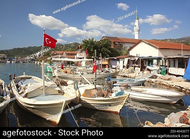 Daily cruise boats anchored inside the harbor near houses and local restaurants in Ucagiz village with the mosque at the background, Demre, Antalya Province
