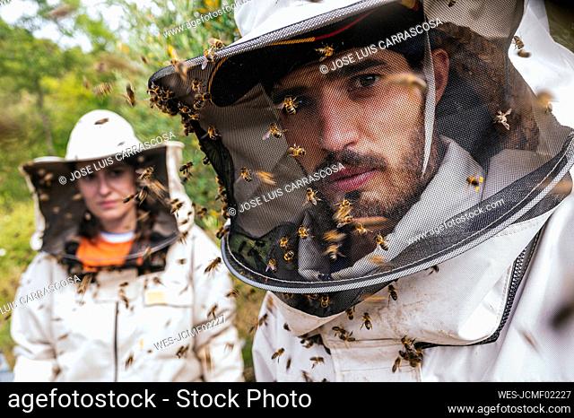 Male and female beekeeper with honey bees on protective suit at farm