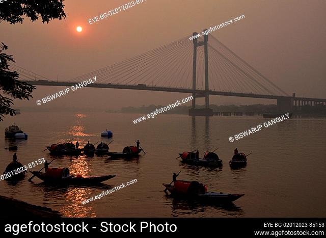 Dec 31, 2022, Kolkata, India. People travel in their boats during the sunset across the  Howrah Bridge (Vidyasagar Setu) On River Ganges