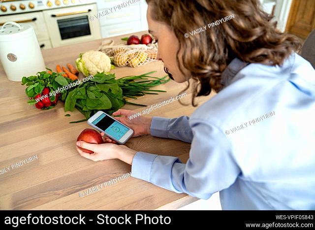 Young woman checking calories of apple on mobile app at home