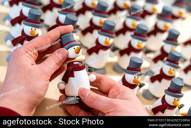 16 October 2021, Saxony, Grünhainichen: Wooden toy maker Stefanie Wendrock from the Hobler company glues parts of the snowman figure Fritz