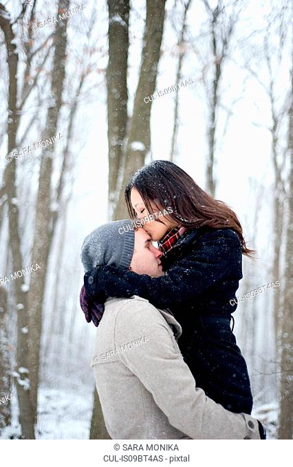 Romantic young woman kissing boyfriend's forehead in snow covered forest, Ontario, Canada
