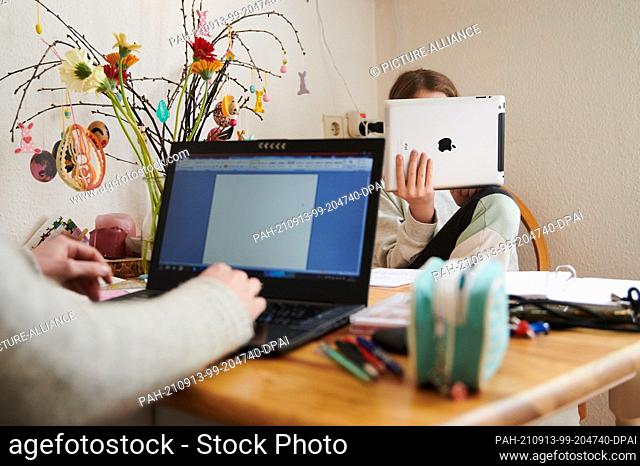 PRODUCTION - 29 April 2021, Berlin: A mother works at the kitchen table while her daughter looks into a tablet across from her