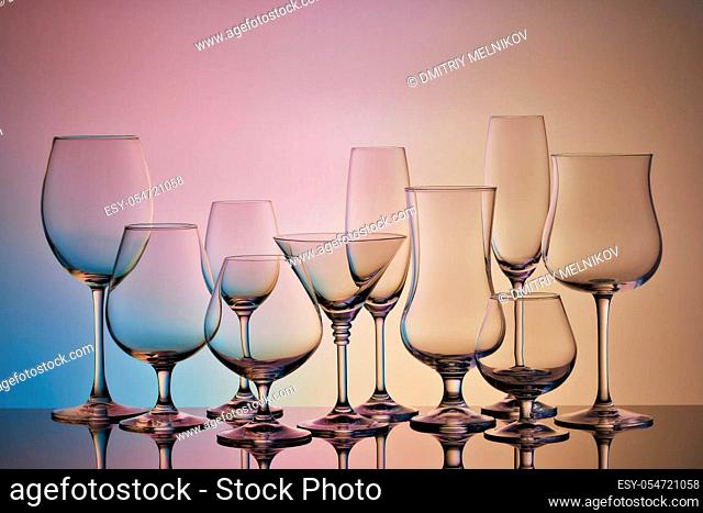 Set of glasses for different alcoholic drinks and cocktails on multicolor gradient background. Empty clear glassware