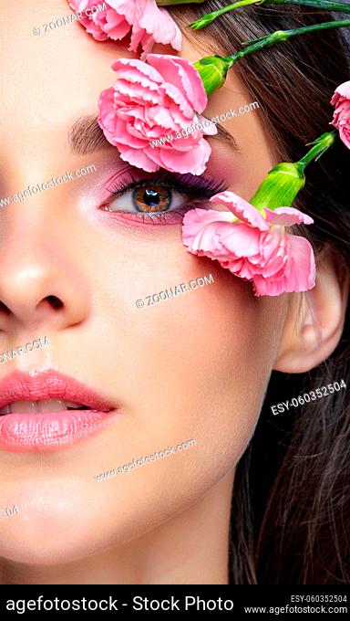 Closeup macro shot of human female face. Woman with natural face and eyes beauty makeup. Pink carnation flowers on the temple