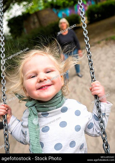 Cheerful girl on swing while grandmother standing at park