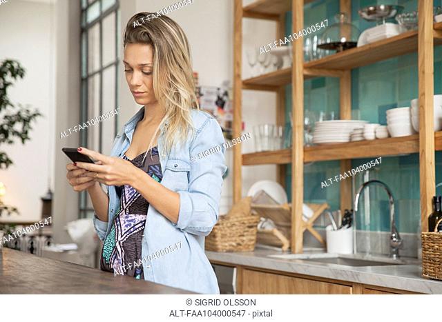 Young woman standing in kitchen with cell phone