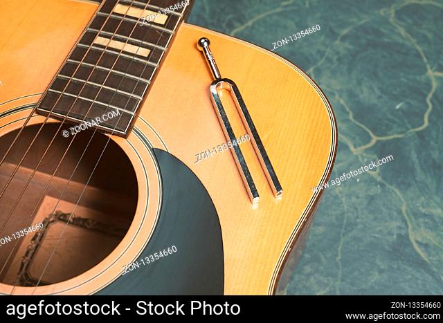 Acoustic guitar on a green marble background, on the guitar there is a tuning fork, music concept
