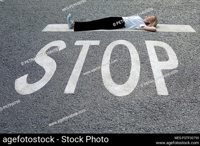 Woman with hands behind head lying down on road at STOP sign