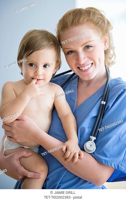 Portrait of female nurse carrying baby boy (12-17 months)
