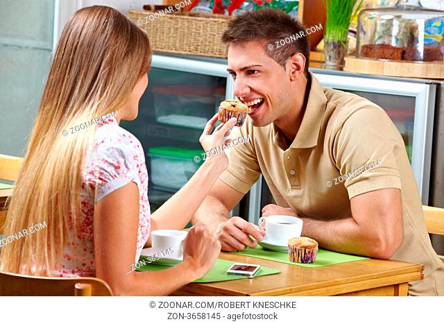 Junge Frau lässt Mann vom Muffin im Café probieren
