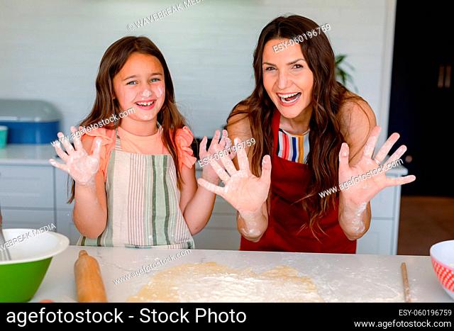 Happy caucasian mother and daughter baking together, showing hands dirty with dough