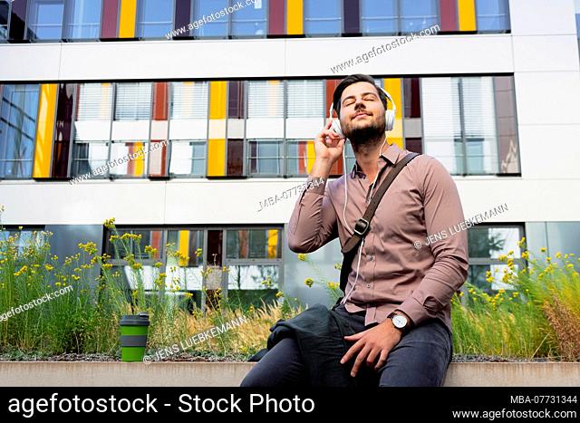 Young man with earphones in front of modern office building, half portrait