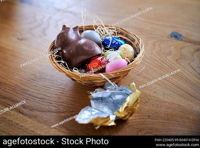PRODUCTION - 01 April 2022, Berlin: ILLUSTRATION - A broken chocolate bunny lies with eggs in an Easter nest. The wrapping is lying next to it