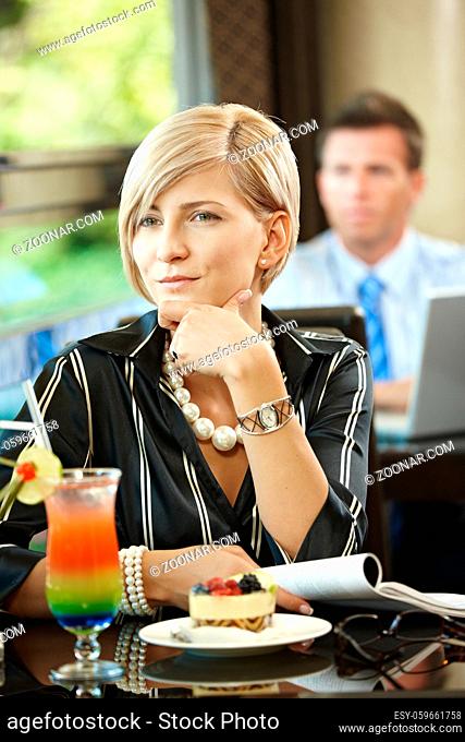 Young woman sitting at table in cafe, reading magazine while waiting for somebody