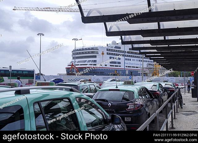 PRODUCTION - 26 October 2023, Portugal, Lissabon: A cruise ship anchors at Lisbon's cruise terminal, while cabs stop at Santa Apolonia station in the Alfama...