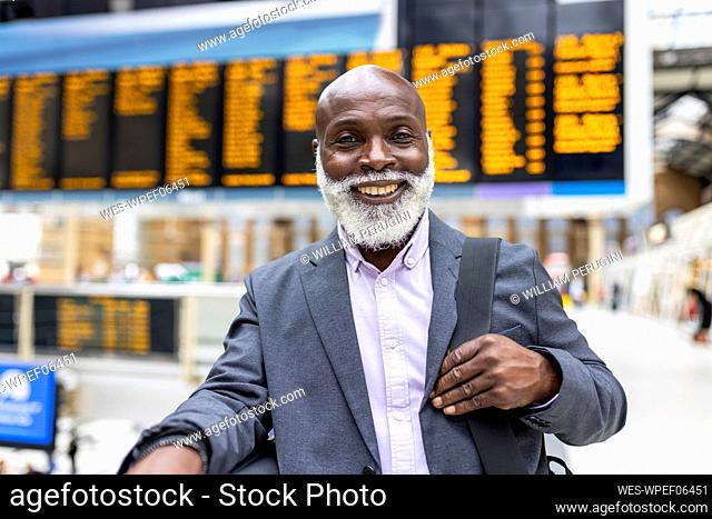 Smiling senior businessman carrying laptop bag at station