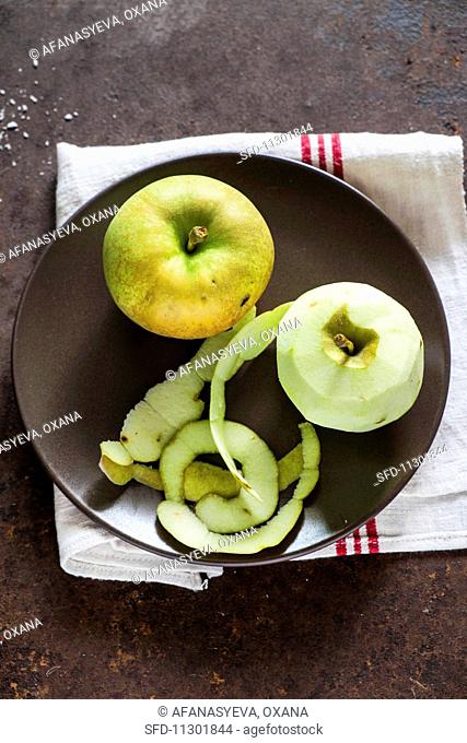 A whole apple and a peeled apple on a plate