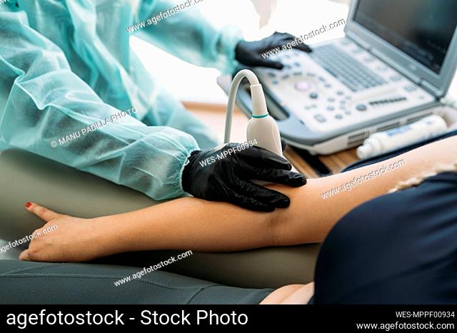 Doctor wearing protective clothes examining woman's arm with ultrasound scanner