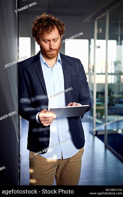Businessman leaning against a wall in office using a tablet