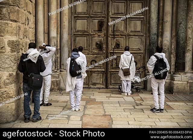 05 April 2020, Israel, Jerusalem: People pray outside the closed door of the Church of the Holy Sepulchre during the Catholic Palm Sunday