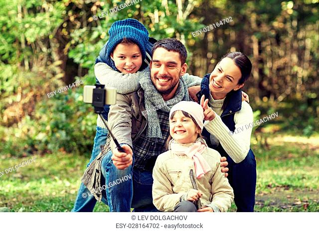 travel, tourism, hike, technology and people concept - happy family taking picture with smartphone selfie stick in woods