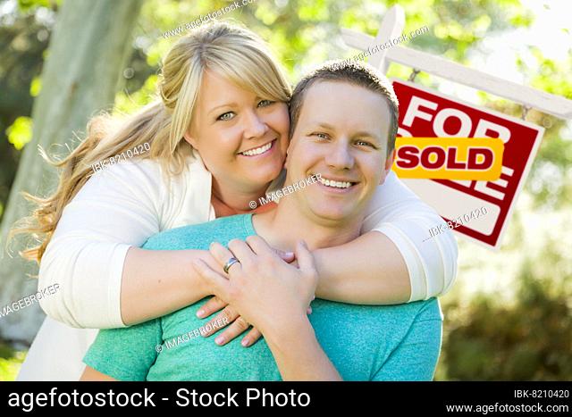Happy couple hug in front of sold real estate sign