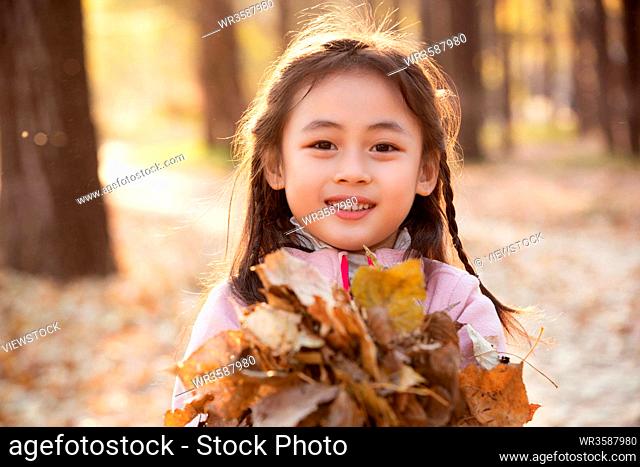 Lovely little girl picking up the leaves in the outdoor