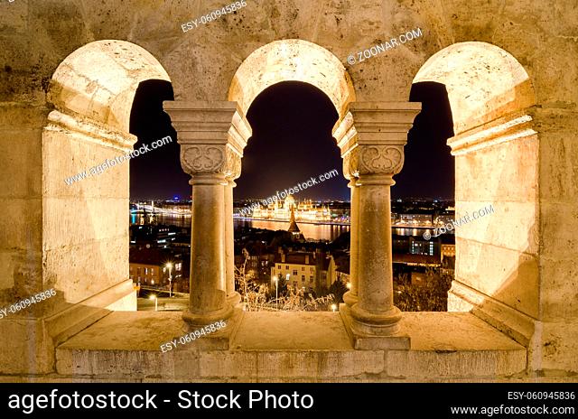 Night view of the famous Hungarian Parliament across the river Danube in Budapest, as seen through the arches of Buda Castle Fishermen's Bastion