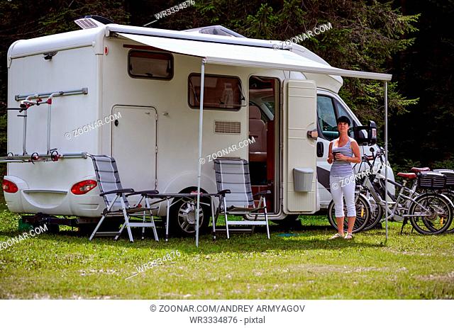 Woman is standing with a mug of coffee near the camper. Caravan car Vacation. Family vacation travel, holiday trip in motorhome RV