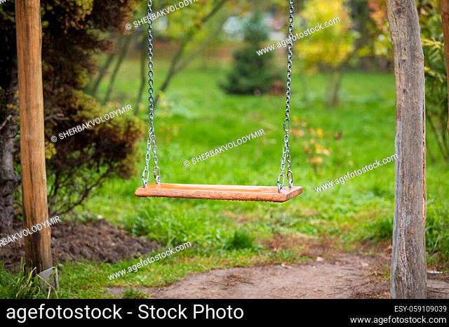 An old wooden swing sitting in a lush backyard. wooden swing on chains at the garden