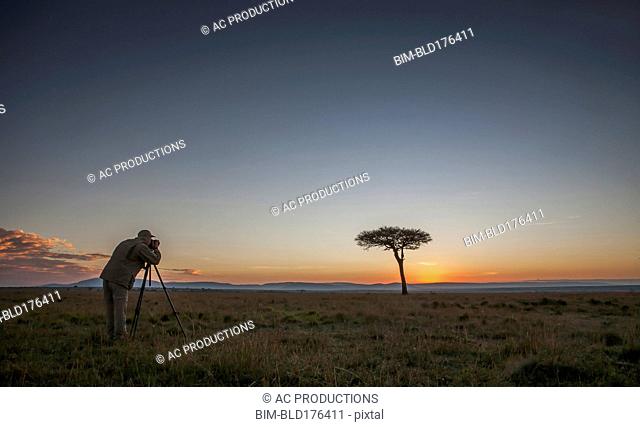 Caucasian photographer photographing tree in savanna