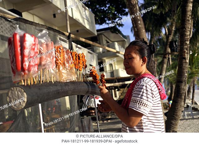 08 December 2018, Philippines, Boracay: A Filipino woman sells skewers of meat on the beach. The beaches of the island of Boracay were closed to the public for...