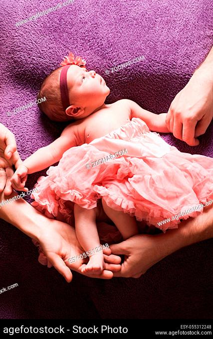 Parents' hands hold a newborn baby girl in pink tutu dress