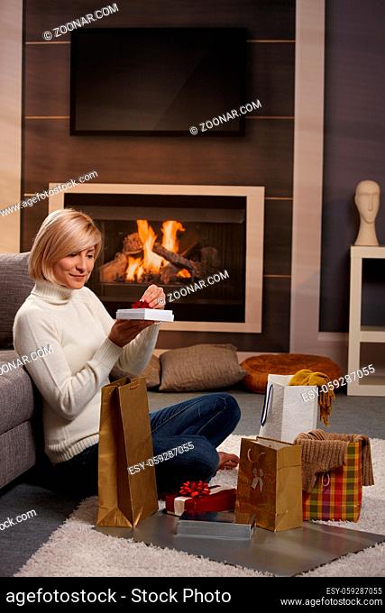 Woman siiting on floor at home in front of fireplace wrapping presents for Chrismas