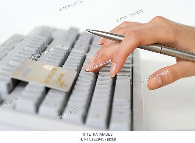 Close up of woman's hand holding pen with credit card and computer keyboard