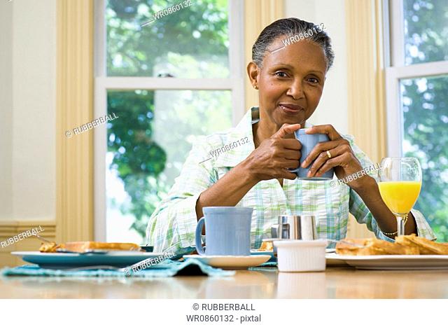 Portrait of a senior woman holding a cup of coffee at the breakfast table