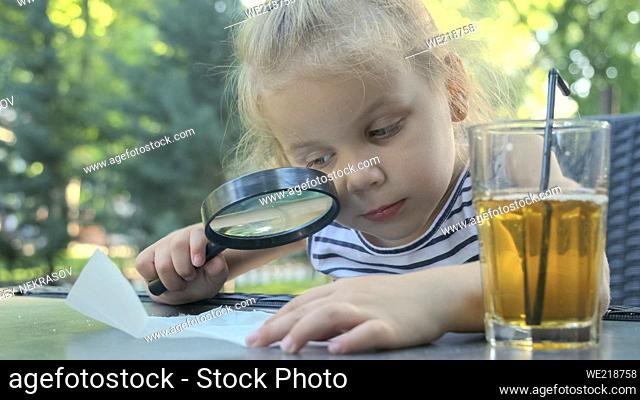 Little girl carefully looks into the lens at the salt. Close-up of blonde girl is studying salt crystals while looking at her through magnifying glass while...