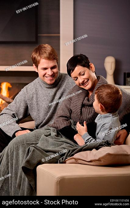 Happy family sitting on sofa at home in front of fireplace, smiling