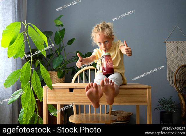 Girl drinking smoothie showing thumbs up gesture sitting on table