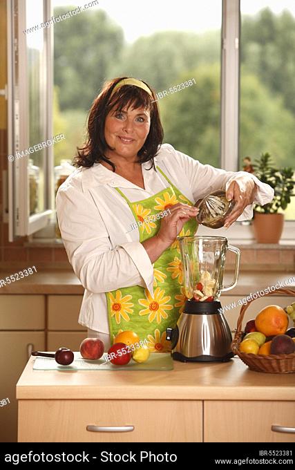Woman pours lemon juice to fruit in blender, prepare, stand blender, mix, pour, pouring, pouring in, add, mix, add to, fruit basket, basket, hair band